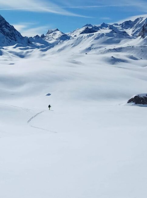 Solo rider boot-packing into an expansive backcountry scene, on a blue-sky day